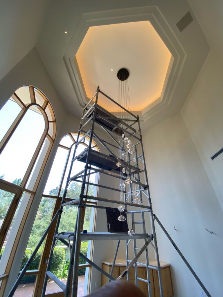 Scaffolding leading up to a large chandelier with large open windows in the background. 